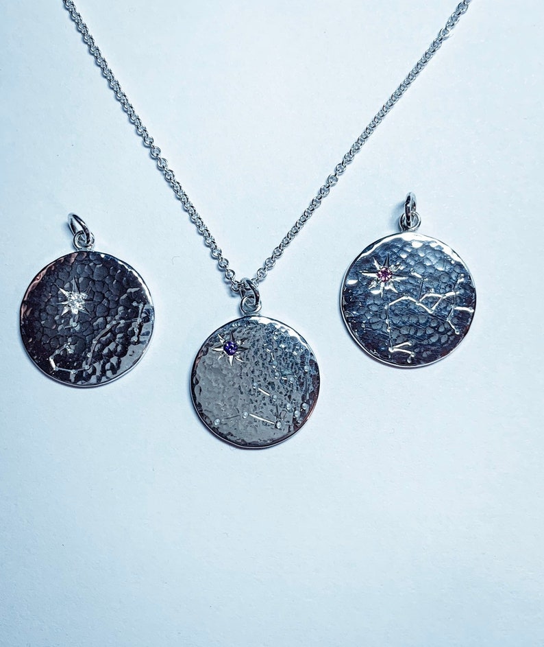 May include: Three silver necklaces with round pendants featuring a star and constellation design. The pendants have a hammered texture and are adorned with small gemstones.