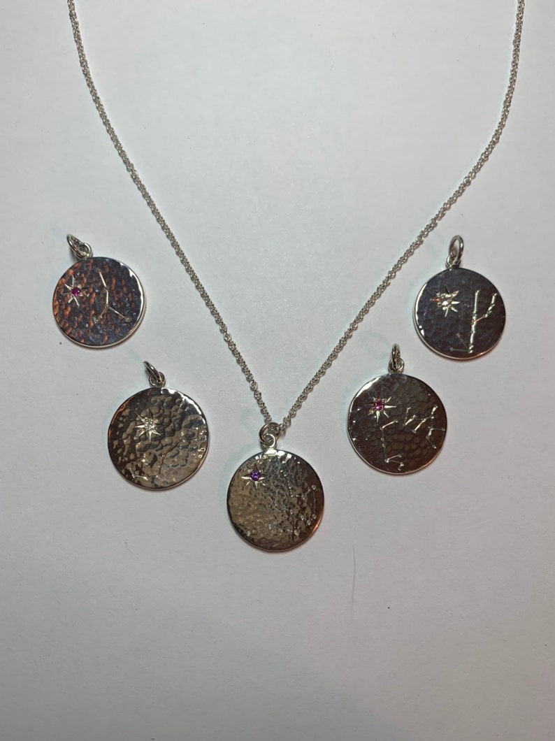 May include: Five silver necklaces with round pendants featuring different star constellations. Each pendant has a small gemstone in the center.
