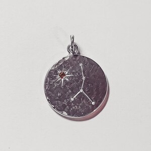 May include: Silver pendant with a hammered finish featuring the Cancer constellation and a small orange gemstone.