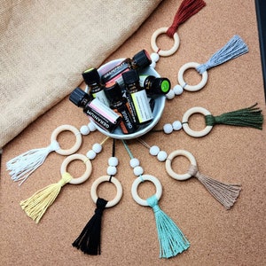 May include: A wooden bead garland with wooden rings and colorful tassels. The garland is decorated with essential oil bottles labeled "Grapefruit", "Orange", and "Geranium".