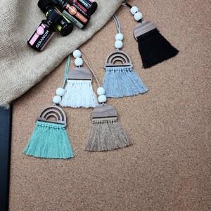Puede incluir: Cinco ambientadores de coche con forma de arcoíris con detalles de madera y flecos de borla. Las borlas son de color negro, blanco, azul claro, verde claro y beige.