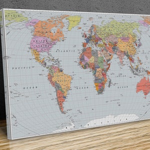 May include: A canvas print of a world map, featuring a light grey background and a detailed representation of continents and countries in various colours. The map includes labels for oceans and major landmasses, with a white border.