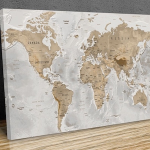 May include: A world map canvas print in neutral tones. The map displays detailed geographical features, including country names and ocean labels. Continents are depicted in a warm brown shade against a light grey backdrop, creating a textured, three-dimensional effect.
