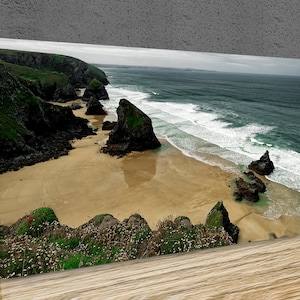 May include: A panoramic view of a rocky coastline with a sandy beach and crashing waves. The beach is surrounded by green cliffs and rocky outcroppings. The sky is overcast and the water is a deep blue.