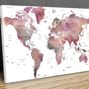May include: A world map print with a watercolour effect. The map features pink, purple, and brown tones, with country names and ocean labels in black. The canvas is displayed on a wooden surface.