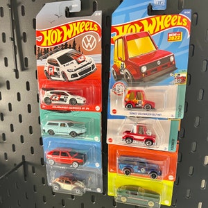 May include: A collection of Hot Wheels toy cars on display. The cars are in their original packaging, featuring various Volkswagen models. The packaging includes the Hot Wheels logo, car names, and the text "NEW FOR 2022". The cars are in various colors, including red, white, and blue.