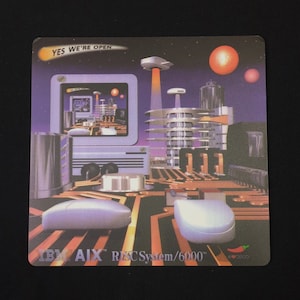 May include: A purple and blue computer mouse pad with a futuristic city scene and the text "YES WE'RE OPEN". The pad also features the text "IBM AIX RSC System/6000".