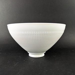 May include: A white, textured bowl with a grid pattern on the lower portion. The bowl has a wide opening and tapers to a small, circular base. The bowl is made of a solid white material.