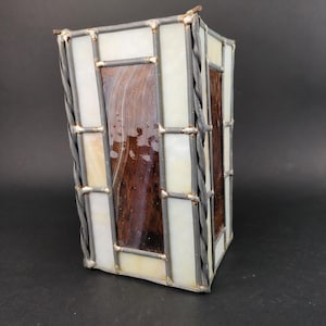 May include: A stained glass lampshade with a geometric design. The lampshade is made of white and brown glass pieces, and the frame is made of metal.