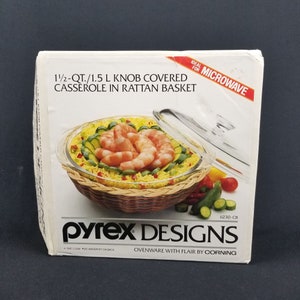 May include: A Pyrex Designs 1 1/2 quart casserole dish with a glass lid in a woven rattan basket. The dish is microwave safe and features a knob on the lid. The dish is filled with cooked rice, shrimp, and zucchini.