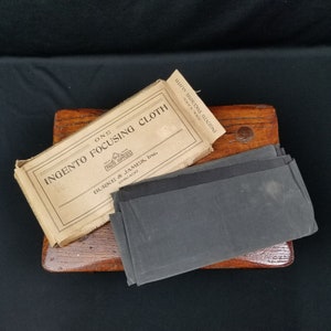 May include: A brown cardboard box with the text "Ingento Focusing Cloth" and "Burke & James, Inc. Chicago" on it. The box is open and a stack of black focusing cloths is visible.