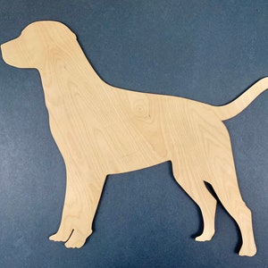 Puede incluir: Un recorte de madera de una silueta de perro. El perro está de pie con la cola enroscada. El recorte está hecho de madera marrón claro.