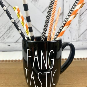 Puede incluir: Taza de cer&aacute;mica negra con texto blanco que dice "Fangtastic". La taza est&aacute; llena de pajitas de papel rayadas de color negro y naranja.