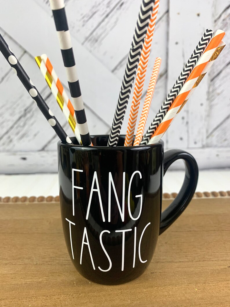 Puede incluir: Taza de cer&aacute;mica negra con texto blanco que dice "Fangtastic". La taza est&aacute; llena de pajitas de papel rayadas de color negro y naranja.
