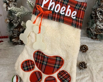 May include: Red and white plaid Christmas stocking with a white faux fur body, a paw print design, and the name "Phoebe" embroidered on the cuff.