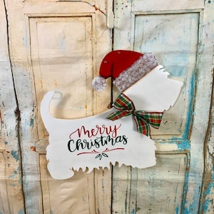 May include: White wooden cutout of a dog wearing a red Santa hat with a white fur trim and a green and red plaid bow. The cutout says "Merry Christmas" in green and red lettering.
