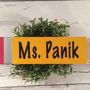 May include: A yellow wooden pencil with a red and silver eraser, painted with the text "Ms. Panik".