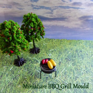 May include: Miniature BBQ grill mould with two ears of corn and two red items on the grill. Two green trees with red berries are in the background. The text "Miniature BBQ Grill Mould" is at the bottom.