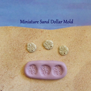 May include: A light purple silicone mould with three sand dollar impressions, and three finished sand dollar castings. The text "Miniature Sand Dollar Mold" is displayed above the objects. The sand dollars are a metallic silver colour.