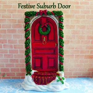 May include: A miniature red door with a green wreath and a red bow, framed by green garland and red ribbon. The door is set against a brick wall and sits on a snowy base. The text "Festive Suburb Door" is at the top.