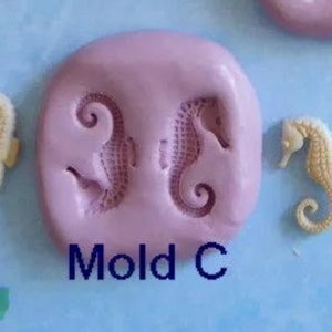 K&ouml;nnte beinhalten: Auf hellblauem Hintergrund befindet sich eine rosa Form mit zwei Seepferdchen-Abdr&uuml;cken und zwei separaten Seepferdchen-Figuren. Der Text "Mold C" ist blau gedruckt. Ein gr&uuml;ner Fisch ist ebenfalls zu sehen.