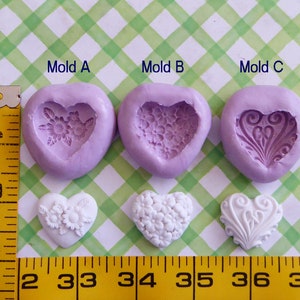 May include: Three heart-shaped silicone molds with floral and decorative designs, alongside three white heart-shaped castings. The molds are labeled Mold A, Mold B, and Mold C. A yellow measuring tape is in the image.