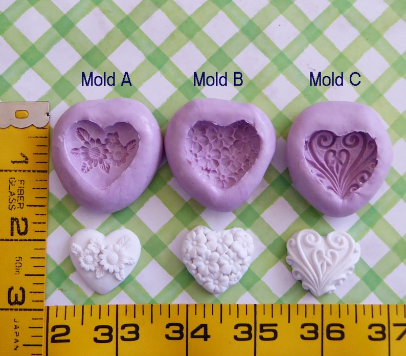 May include: Three heart-shaped silicone molds with floral and decorative designs, alongside three white heart-shaped castings. The molds are labeled Mold A, Mold B, and Mold C. A yellow measuring tape is in the image.