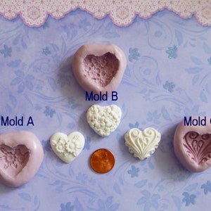 May include: Three heart-shaped molds labeled A, B, and C, with a white heart-shaped object and a penny. Mold A is pink with a floral design. Mold B is pink with a lace design. Mold C is pink with a decorative design.