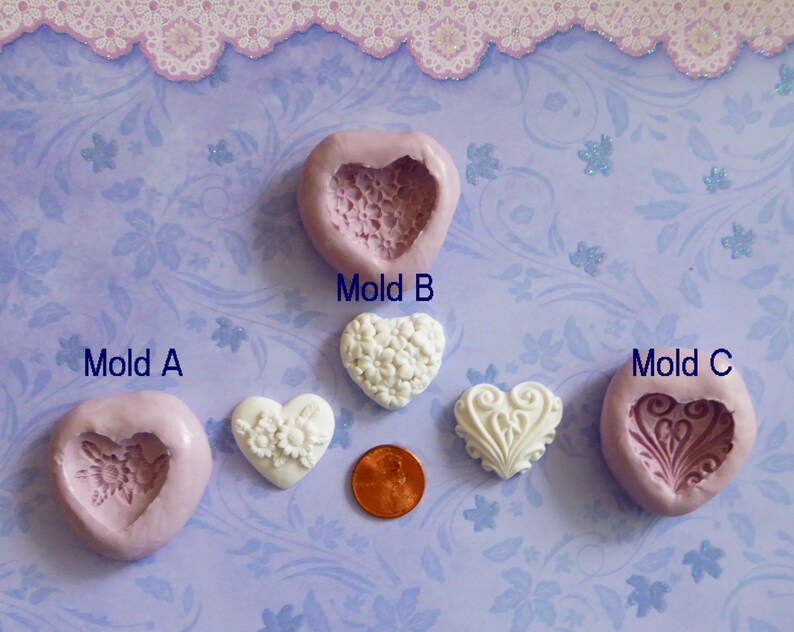 May include: Three heart-shaped molds labeled A, B, and C, with a white heart-shaped object and a penny. Mold A is pink with a floral design. Mold B is pink with a lace design. Mold C is pink with a decorative design.