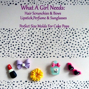 May include: An assortment of miniature accessories including a red lipstick, a purple bow, a yellow scrunchie, a perfume bottle, and pink heart-shaped sunglasses. The text "What A Girl Needs" is displayed above the accessories.