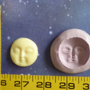 May include: A yellow, smiling moon face and a pink mold of the same face are displayed. The moon face is approximately 1 inch in diameter. A yellow measuring tape is in the image, with measurements in inches.