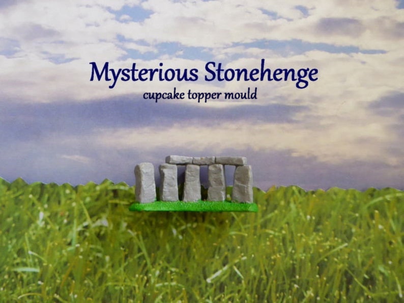 May include: A miniature Stonehenge cupcake topper mold. The mold is gray and green, with the text "Mysterious Stonehenge" and "cupcake topper mould" in blue. The background features a grassy field and a cloudy sky.