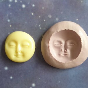 May include: A yellow, circular moon face with closed eyes sits next to a pink, oval-shaped mold of a moon face. The moon face has a serene expression. The background is a dark blue with white speckles.