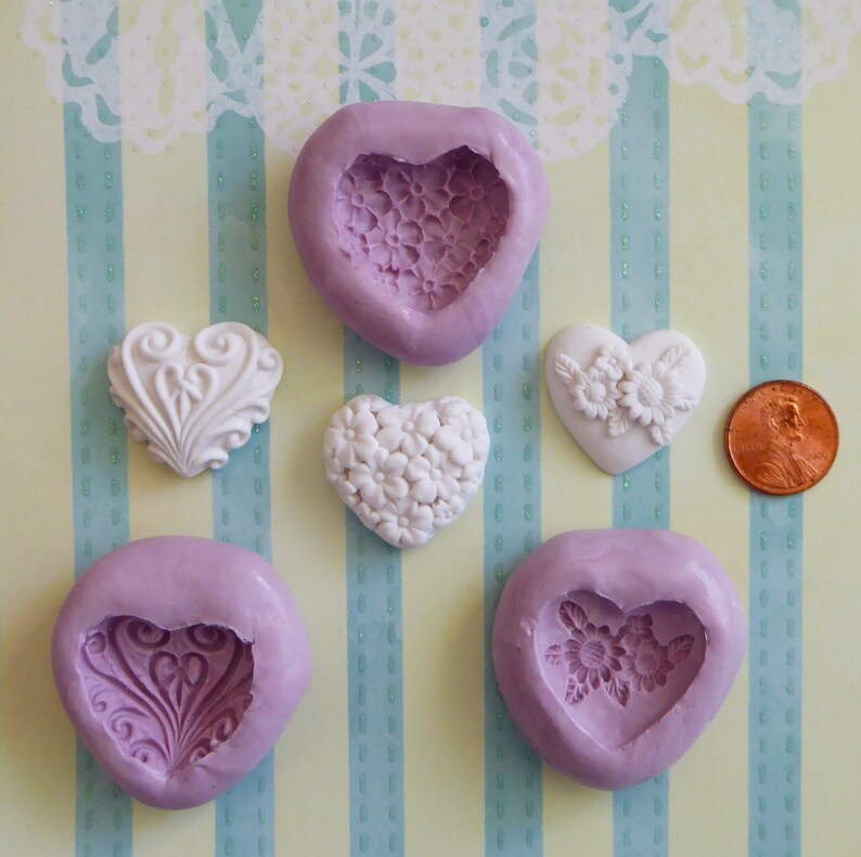 May include: An assortment of heart-shaped molds and decorative heart embellishments. The molds are lavender, with floral and ornate designs. The embellishments are white, featuring floral and scrollwork patterns. A penny is included for size reference.