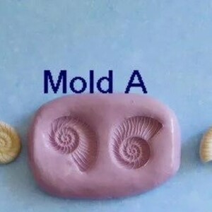 K&ouml;nnte beinhalten: Eine hellrosa Silikonform mit der Aufschrift "Mold A" mit zwei Muschelabdr&uuml;cken und zwei fertigen Muschelgussteilen. Die Muscheln sind cremefarben. Der Hintergrund ist hellblau.