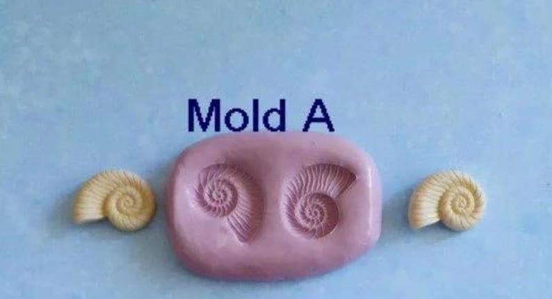 K&ouml;nnte beinhalten: Eine hellrosa Silikonform mit der Aufschrift "Mold A" mit zwei Muschelabdr&uuml;cken und zwei fertigen Muschelgussteilen. Die Muscheln sind cremefarben. Der Hintergrund ist hellblau.