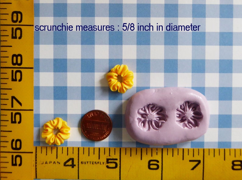May include: Yellow scrunchies, each approximately 0.625 inches in diameter, are displayed with a penny and a lilac-colored mold. The text reads "scrunchie measures: 5/8 inch in diameter". The items are on a blue and white checkered background.