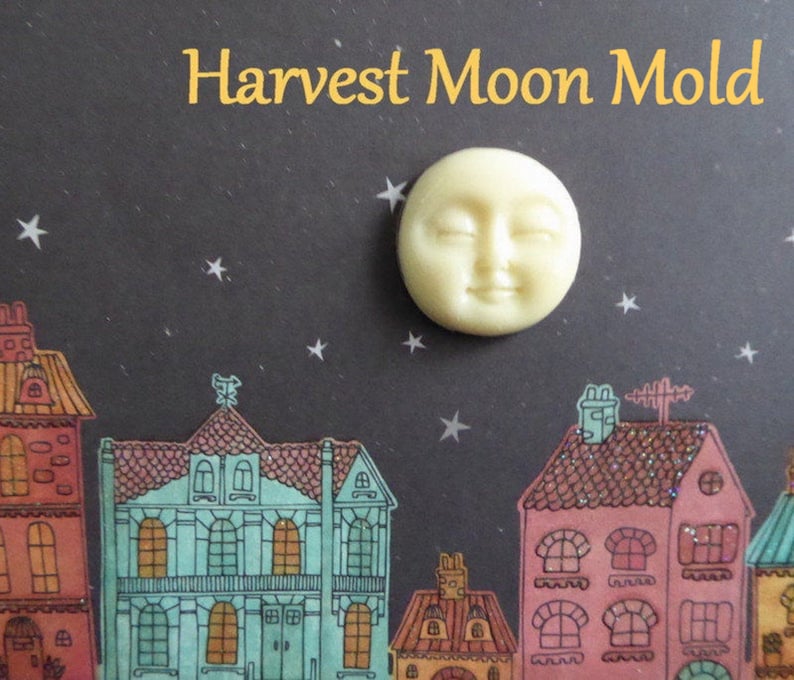 May include: A cream-colored Harvest Moon Mold with a smiling face, set against a dark background with a starry night sky and colorful illustrated houses. The text "Harvest Moon Mold" is in gold.