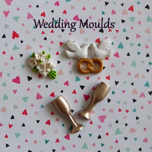 May include: Assorted wedding-themed molds. Includes a bouquet, two doves, interlocking rings, and two champagne flutes. The background is a white surface with a pattern of hearts in various colors. The text "Wedding Moulds" is at the top.