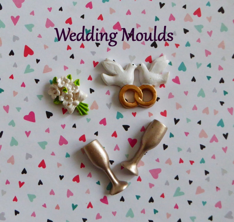 May include: Assorted wedding-themed molds. Includes a bouquet, two doves, interlocking rings, and two champagne flutes. The background is a white surface with a pattern of hearts in various colors. The text "Wedding Moulds" is at the top.