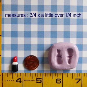May include: A miniature lipstick figurine with a red top, white band, and black base, next to a penny and a lavender mold. The text in the image says "measures: 3/4 x a little over 1/4 inch".