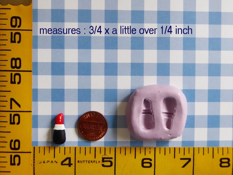 May include: A miniature lipstick figurine with a red top, white band, and black base, next to a penny and a lavender mold. The text in the image says "measures: 3/4 x a little over 1/4 inch".