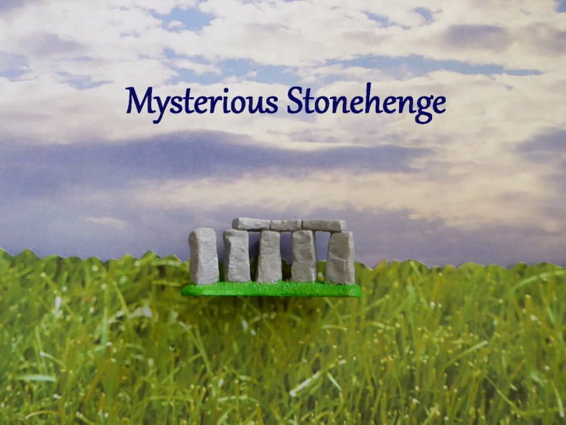 May include: A miniature model of Stonehenge, featuring gray stone structures on a green base, set against a backdrop of a grassy field and a cloudy sky. The text "Mysterious Stonehenge" is displayed above the model.