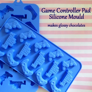 May include: Blue silicone mould for making chocolates, featuring game controller and "Level Up" designs. The text "Game Controller Pad Silicone Mould" and "makes glossy chocolates" are visible on the image.