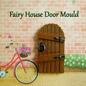 May include: A brown wooden fairy house door mould with black hardware. The text "Fairy House Door Mould" is above the door. A red bicycle with a basket of pink flowers is to the left of the door.