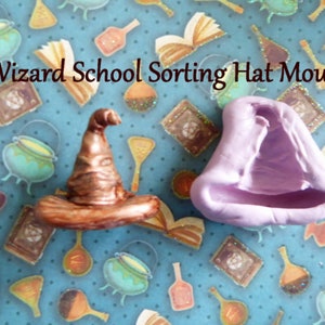 May include: A Wizard School Sorting Hat Mould is displayed. The image shows a bronze-colored sorting hat and a lavender-colored hat-shaped mould. The background is a light blue pattern with illustrations of cauldrons, books, and potions. Text on the image reads "Wizard School Sorting Hat Mould."