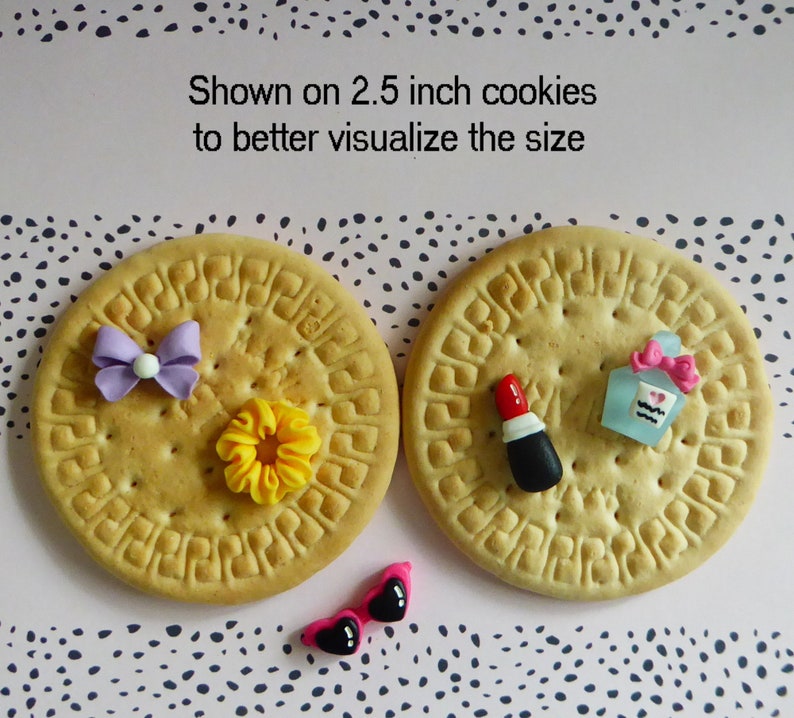 May include: Two 2.5-inch cookies with decorative elements. One cookie has a purple bow and yellow flower. The other has a lipstick and perfume bottle. Pink sunglasses with black hearts are also present. Text on the image reads: Shown on 2.5 inch cookies to better visualize the size.
