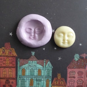 May include: A lavender silicone mold and a yellow moon-shaped resin piece with closed eyes. The mold is round with a recessed moon face. The resin moon has a smiling face. The background features a night sky with stars and colorful houses.