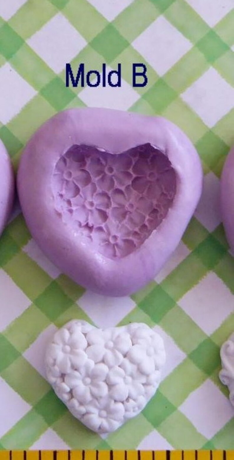 May include: A lavender heart-shaped mold with a floral pattern, labeled "Mold B". Below, a white heart-shaped object with a floral design is visible. The background features a green and white checkered pattern.