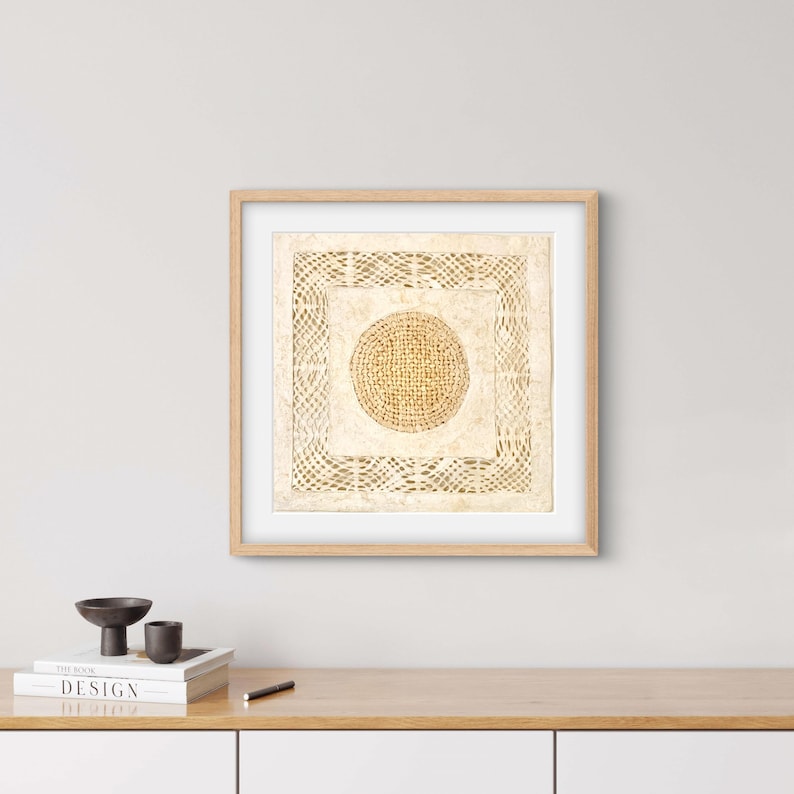 May include: A framed beige and brown abstract art print with a circular design in the center. The print is in a light wood frame and is hanging on a white wall.